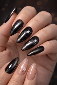 Glossy black galaxy almond nails with white shooting star accents and subtle shimmer, plus nude accent nails with tiny daisy detail, Nail Trends 2026 at Top Nails 3 Airdrie