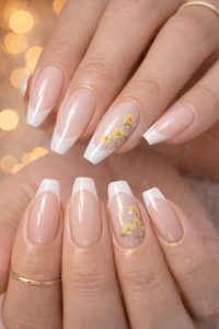 Glossy nude coffin nails with crisp white French tips, subtle shimmer, and tiny yellow daisy floral accents on feature nails, Nail Trends 2026 at Top Nails 3 Airdrie